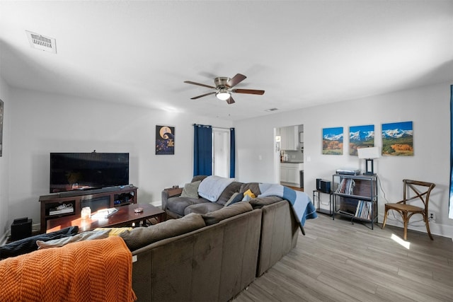 living area featuring baseboards, light wood finished floors, visible vents, and a ceiling fan