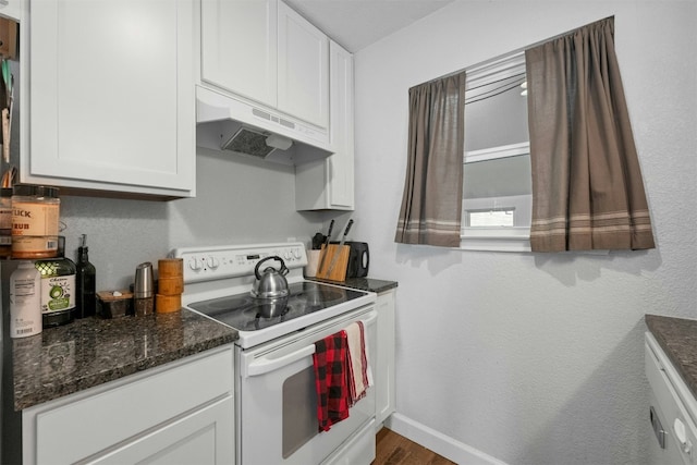 kitchen featuring baseboards, white cabinets, dark stone counters, under cabinet range hood, and white range with electric cooktop