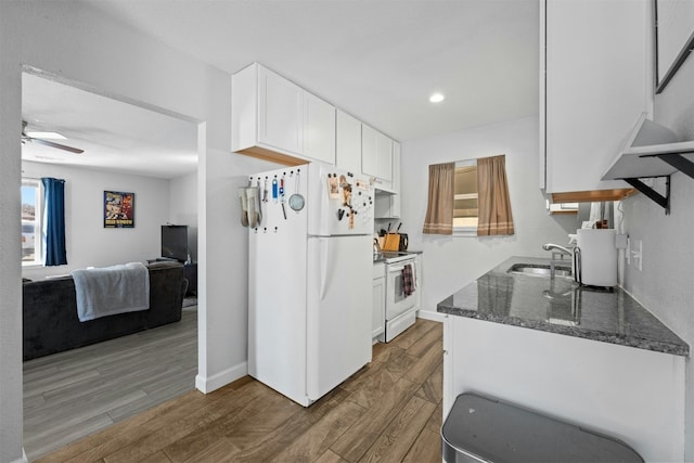 kitchen featuring white appliances, dark stone counters, wood finished floors, white cabinetry, and a sink