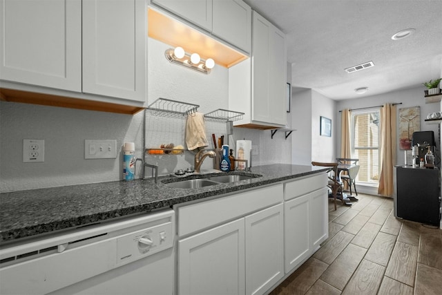 kitchen with white dishwasher, a sink, visible vents, white cabinets, and wood tiled floor