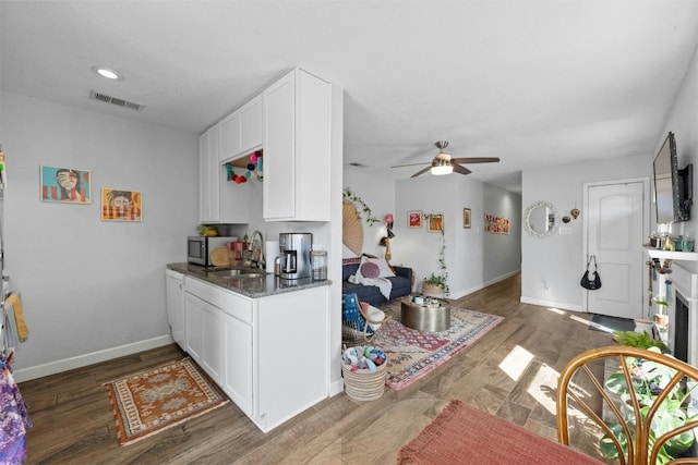 kitchen featuring wood finished floors, a sink, visible vents, white cabinetry, and stainless steel microwave