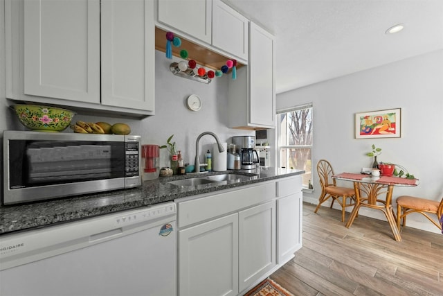 kitchen featuring light wood finished floors, stainless steel microwave, a sink, dark stone countertops, and dishwasher