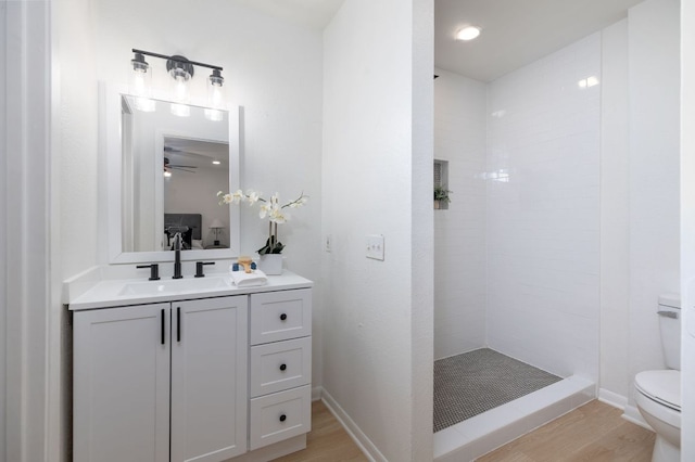 bathroom featuring toilet, vanity, wood finished floors, and tiled shower