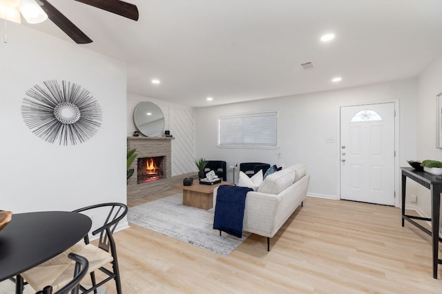 living room featuring recessed lighting, visible vents, light wood-type flooring, a lit fireplace, and baseboards