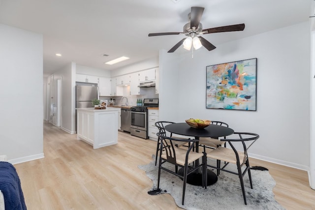 kitchen with stainless steel appliances, light wood-style flooring, white cabinetry, under cabinet range hood, and baseboards