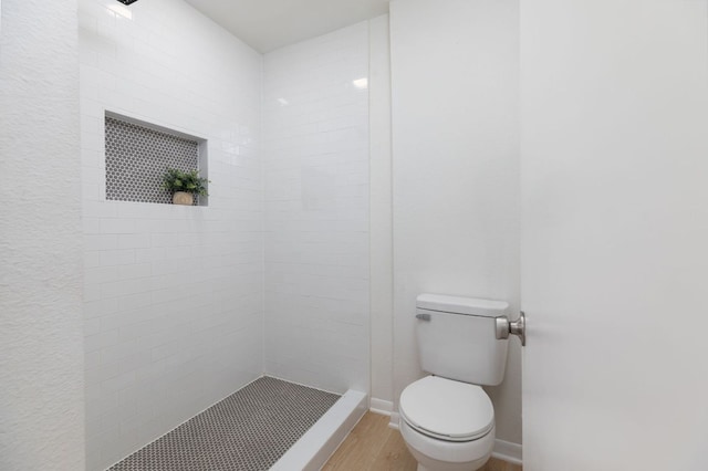 full bathroom with baseboards, a tile shower, toilet, and wood finished floors