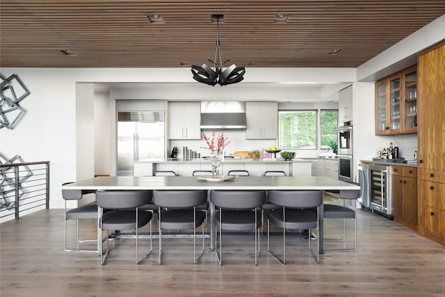 719 Cutlass St, Austin, TX 78734 - kitchen featuring wall chimney range hood, wine cooler, appliances with stainless steel finishes, a kitchen breakfast bar, and wooden ceiling