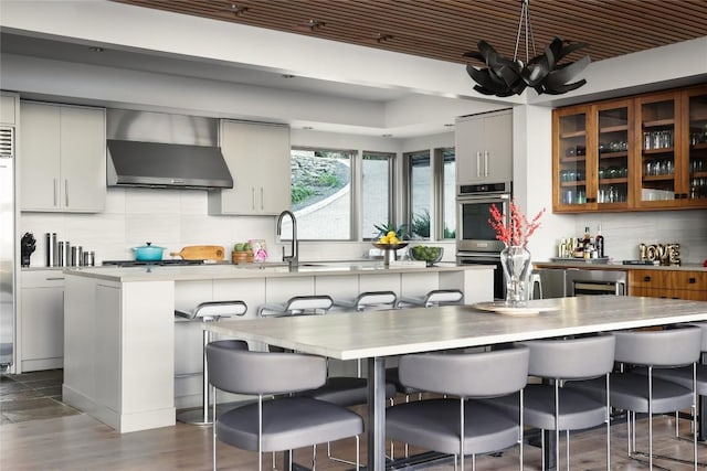 719 Cutlass St, Austin, TX 78734 - kitchen featuring wall chimney range hood, stainless steel appliances, backsplash, light countertops, and a kitchen bar