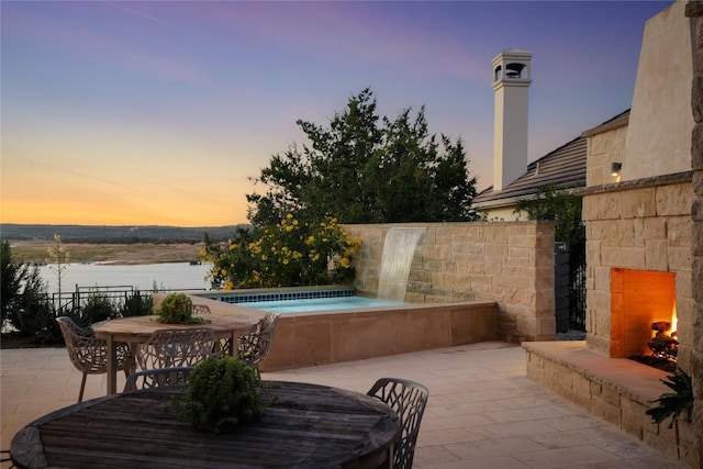 719 Cutlass St, Austin, TX 78734 - patio terrace at dusk with an outdoor stone fireplace, a patio, outdoor dining space, and a jacuzzi