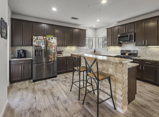 kitchen with a center island, light wood-style flooring, appliances with stainless steel finishes, dark brown cabinetry, and light stone countertops