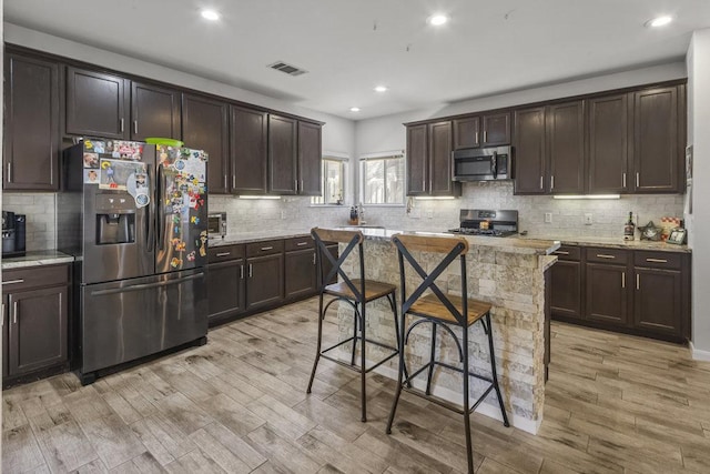 kitchen with dark brown cabinets, appliances with stainless steel finishes, a breakfast bar area, and visible vents