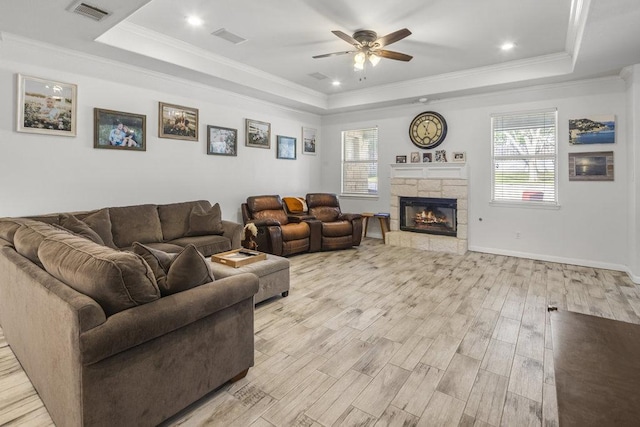 living room with light wood-style floors, visible vents, a raised ceiling, and a stone fireplace