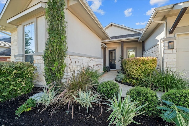 doorway to property featuring stone siding, an attached garage, and stucco siding