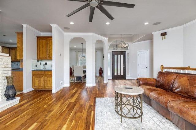 living area featuring baseboards, crown molding, arched walkways, and wood finished floors