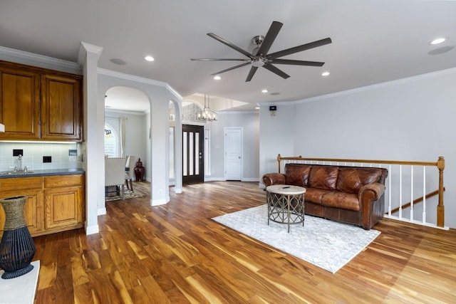 living room featuring baseboards, crown molding, arched walkways, and wood finished floors