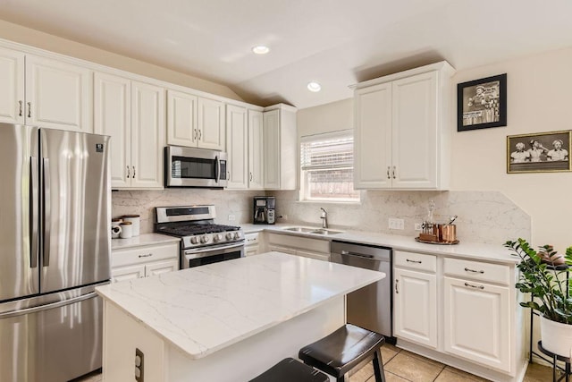 kitchen featuring a center island, lofted ceiling, white cabinets, stainless steel appliances, and a sink