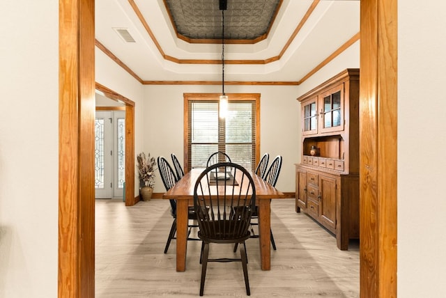 dining space featuring light wood-style flooring, visible vents, a raised ceiling, and crown molding