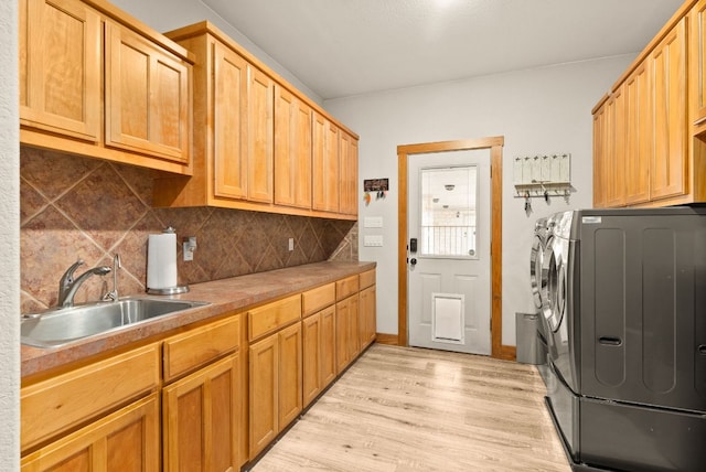 clothes washing area with a sink, baseboards, light wood-style floors, washer and dryer, and cabinet space