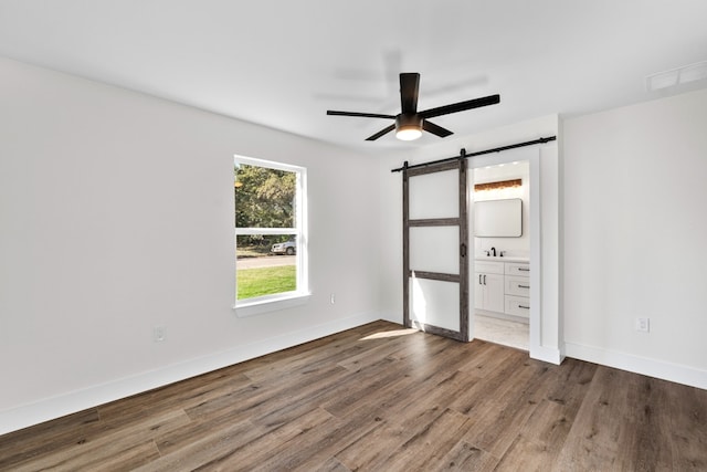 1520 Weyford Dr, Austin, TX 78757 - unfurnished bedroom featuring a barn door, wood finished floors, ensuite bathroom, and a ceiling fan