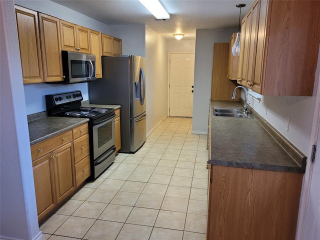 kitchen with appliances with stainless steel finishes, dark countertops, a sink, and light tile patterned flooring