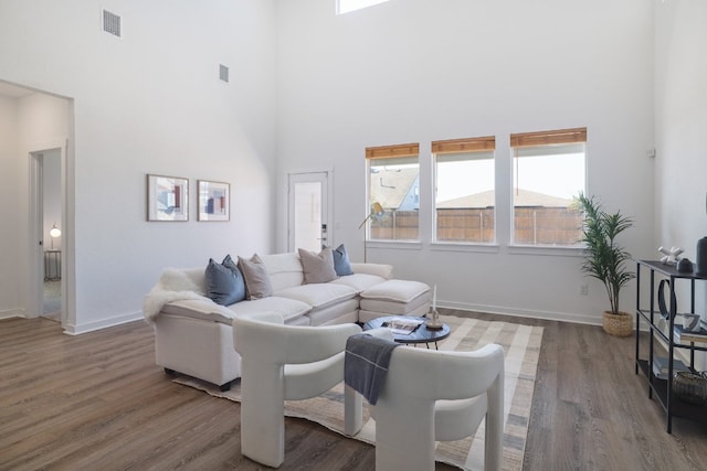 living area with a towering ceiling, baseboards, and wood finished floors