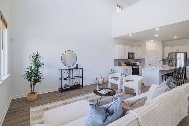 living room with recessed lighting, a high ceiling, baseboards, and wood finished floors