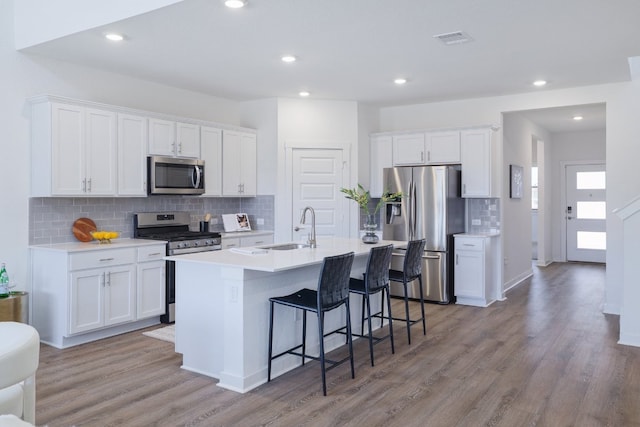 kitchen with a breakfast bar, a kitchen island with sink, stainless steel appliances, white cabinetry, and a sink