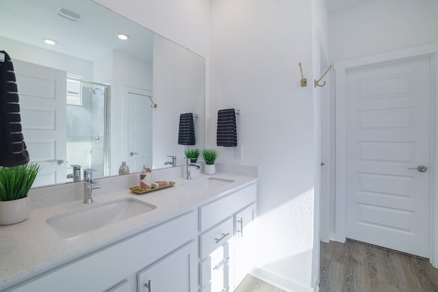 bathroom with double vanity, a shower stall, a sink, and wood finished floors