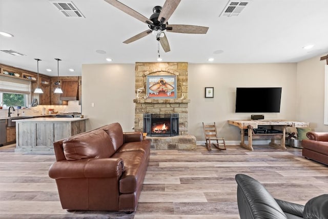 living room featuring light wood-type flooring, a fireplace, and visible vents