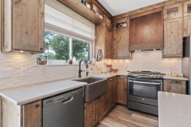 kitchen featuring tasteful backsplash, light wood-style flooring, stainless steel appliances, light countertops, and a sink