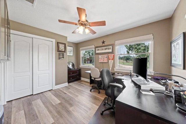 home office featuring light wood-type flooring, a healthy amount of sunlight, visible vents, and a ceiling fan