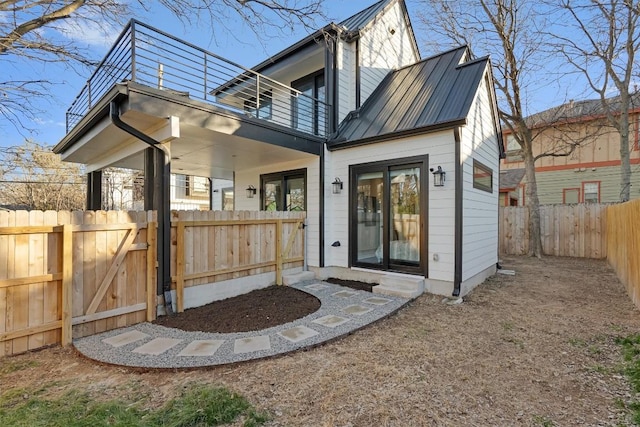 back of house featuring a fenced backyard, metal roof, and a balcony