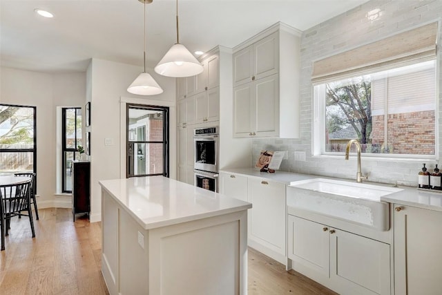 kitchen with stainless steel double oven, light wood-type flooring, a sink, and decorative backsplash