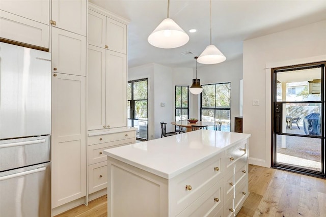 kitchen featuring a kitchen island, visible vents, light wood-style floors, hanging light fixtures, and stainless steel fridge