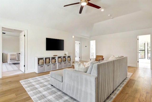 living room featuring light wood-type flooring, baseboards, vaulted ceiling, and a ceiling fan