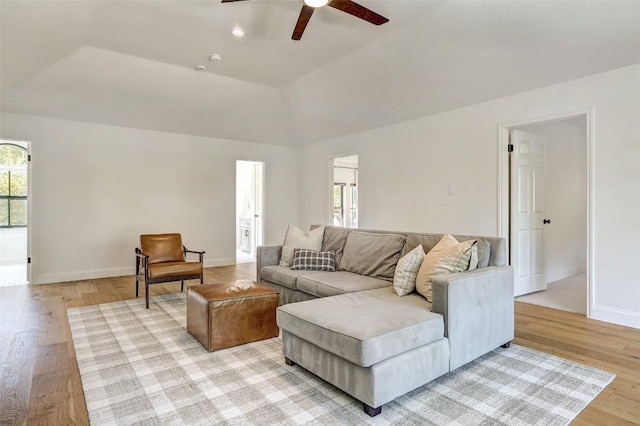 living room with light wood-style floors, a raised ceiling, baseboards, and a ceiling fan