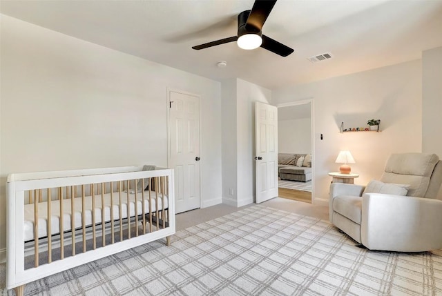 bedroom with ceiling fan, a nursery area, visible vents, and baseboards