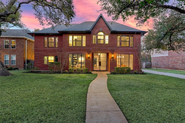 view of front of property featuring roof with shingles, a front yard, and brick siding