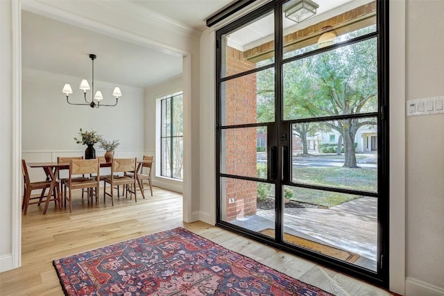 dining area with light wood-style flooring, ornamental molding, a notable chandelier, and wainscoting