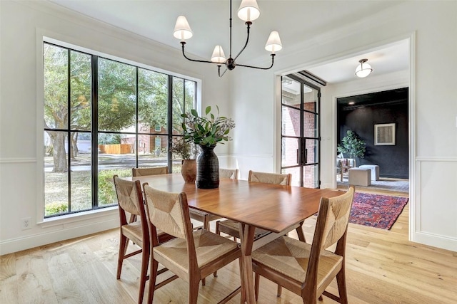 dining room with light wood-type flooring, a healthy amount of sunlight, a notable chandelier, and baseboards