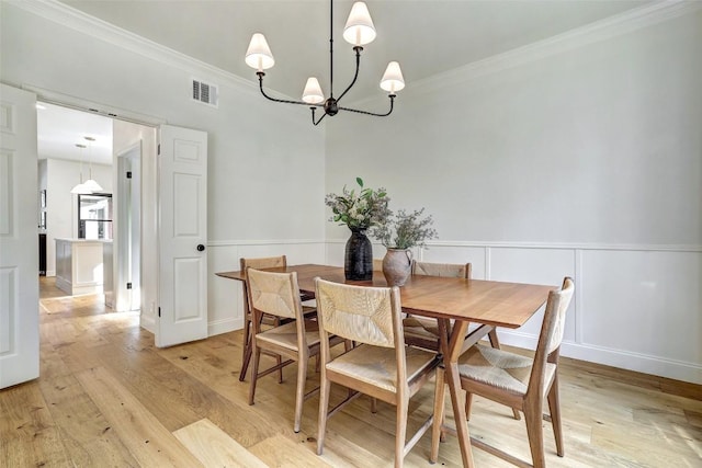 dining space with light wood finished floors, visible vents, crown molding, and wainscoting