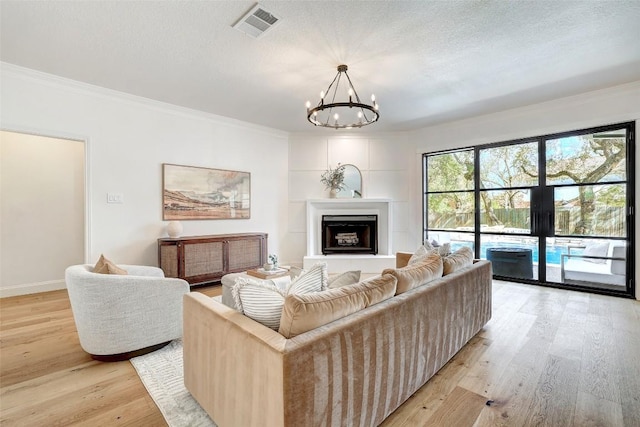 living room with a notable chandelier, visible vents, a fireplace with raised hearth, a textured ceiling, and light wood-type flooring