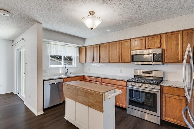 kitchen with decorative backsplash, brown cabinetry, dark wood-type flooring, stainless steel appliances, and a sink