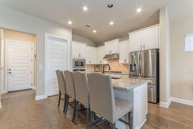 409 Flying Orchid Dr, San Marcos, TX 78666 - kitchen with stainless steel appliances, under cabinet range hood, a breakfast bar, dark wood finished floors, and decorative backsplash