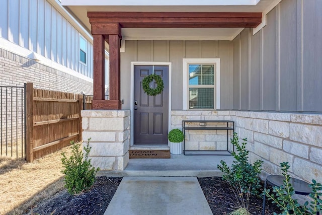 doorway to property with stone siding, board and batten siding, and fence