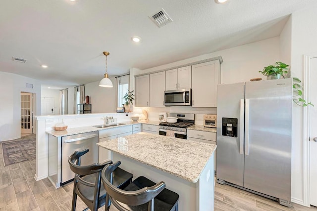 kitchen with a peninsula, appliances with stainless steel finishes, light wood-style flooring, and visible vents