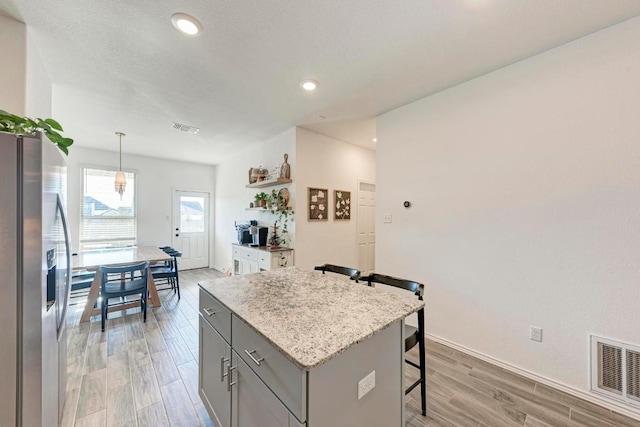 kitchen featuring stainless steel refrigerator with ice dispenser, visible vents, gray cabinetry, light wood-style floors, and a kitchen breakfast bar