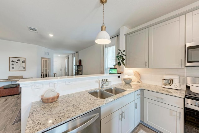 kitchen featuring stainless steel appliances, visible vents, open floor plan, a sink, and a peninsula