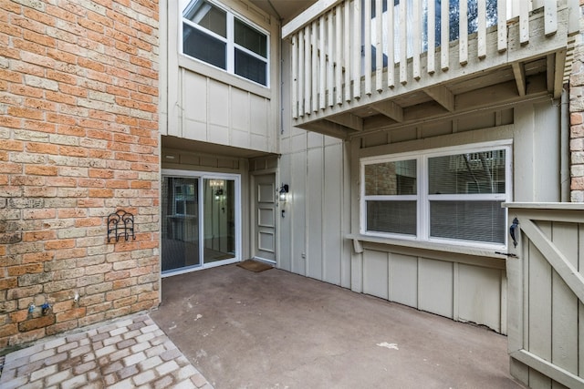 view of exterior entry with a patio area, board and batten siding, and brick siding