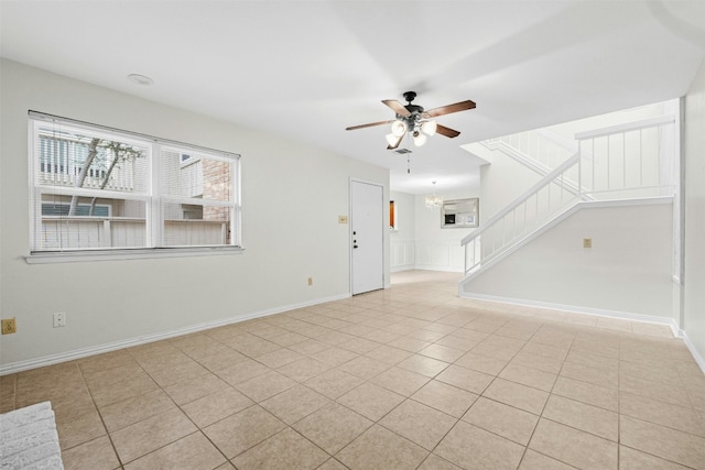 unfurnished living room with stairs, a wealth of natural light, tile patterned flooring, and ceiling fan with notable chandelier